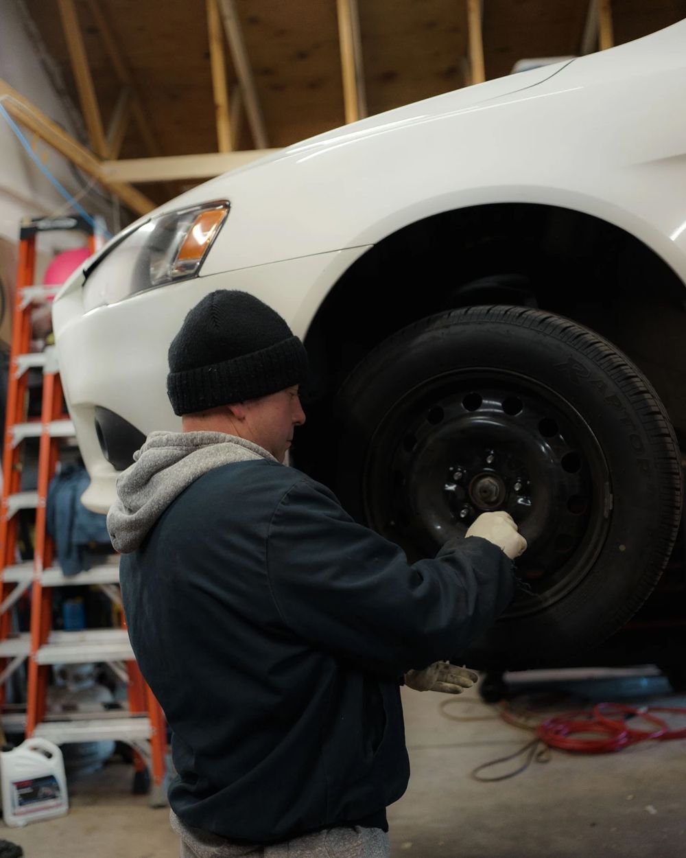 Mechanic removing the front wheel of a white sedan on a lift at Foreign Auto 5280